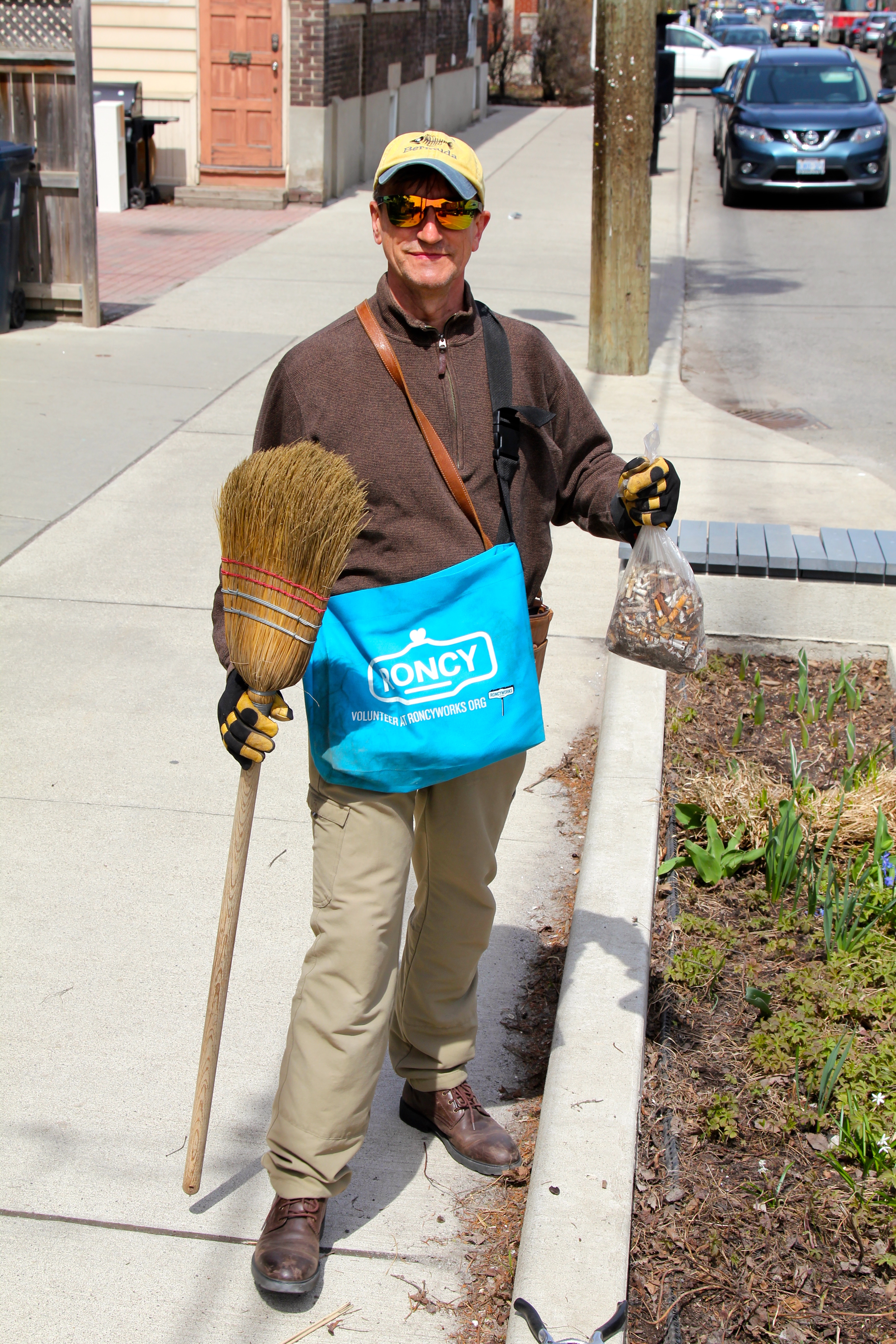 RoncyWorks volunteer holding broom and bag of cigarette litter.